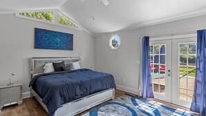 Une chambre à coucher comprenant un lit, une table de chevet, un ventilateur de plafond, une fenêtre et une vue sur l’extérieur.