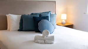 A neatly made bed with rolled towels, a bedside lamp, and a nightstand with a lamp.