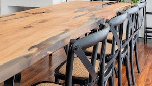 A modern dining area with a wooden table, black chairs, a mounted TV, and a potted plant.