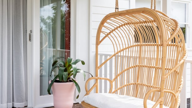 A wicker swing chair with a white cushion on a wooden deck.