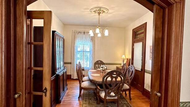 Uma sala de jantar com mesa de madeira, cadeiras e um lustre.