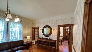 Sala de estar com sofá, mesa de centro, piso de madeira, tapete estampado, lustre e espelho na parede.