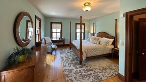 Quarto com cama de dossel, um espelho grande, cômoda de madeira e janela com vista.