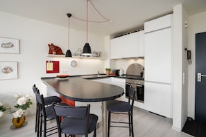 A modern kitchen with a curved island, white cabinetry, and a black countertop. There are two chairs at the island, a clock on the wall, and a phone on the door.