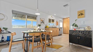 A modern kitchen with a dining area, large windows, and a view of the sea. - The Hidalgo House (Desert Hot Springs)