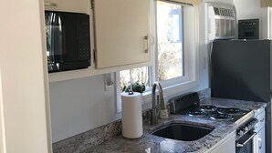 Una cocina con armarios blancos, encimera de granito, pileta de acero inoxidable, estufa y microondas.