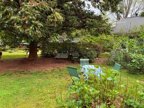 A garden with a large tree, a swing, and a table with chairs. - The Guest House at Elon Cottage (Gibsonville)