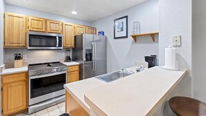 Una cocina moderna con armarios de madera, electrodomésticos de acero inoxidable, una encimera blanca y una pequeña isla con un fregadero.