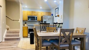 Un comedor con una mesa y sillas de madera, una cocina al fondo y una escalera que sube a otro nivel.