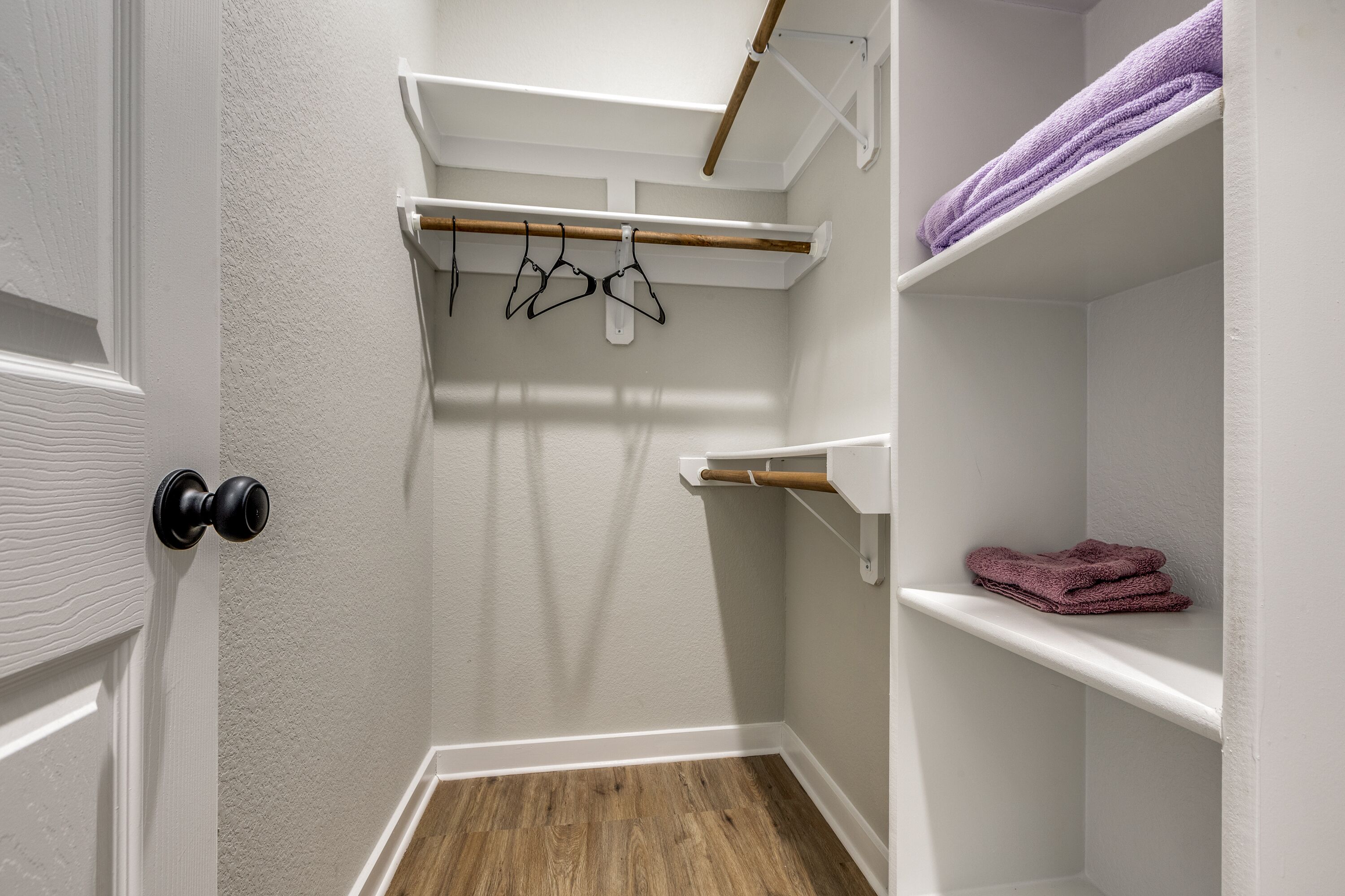 Un vestidor con paredes blancas, suelo de madera y estantes para guardar objetos.