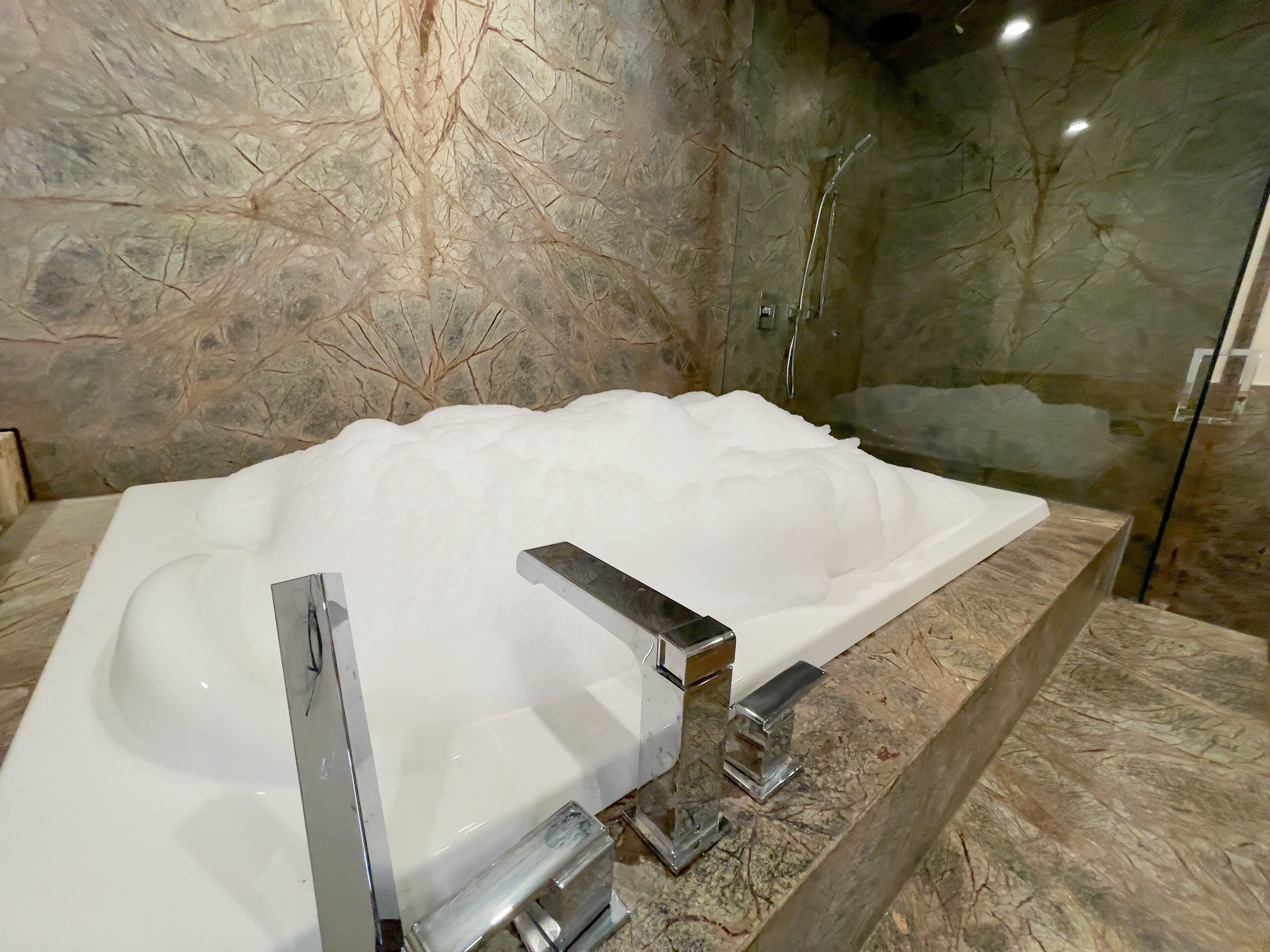 Une salle de bain moderne avec une grande baignoire, des murs en marbre et une cabine de douche en verre.