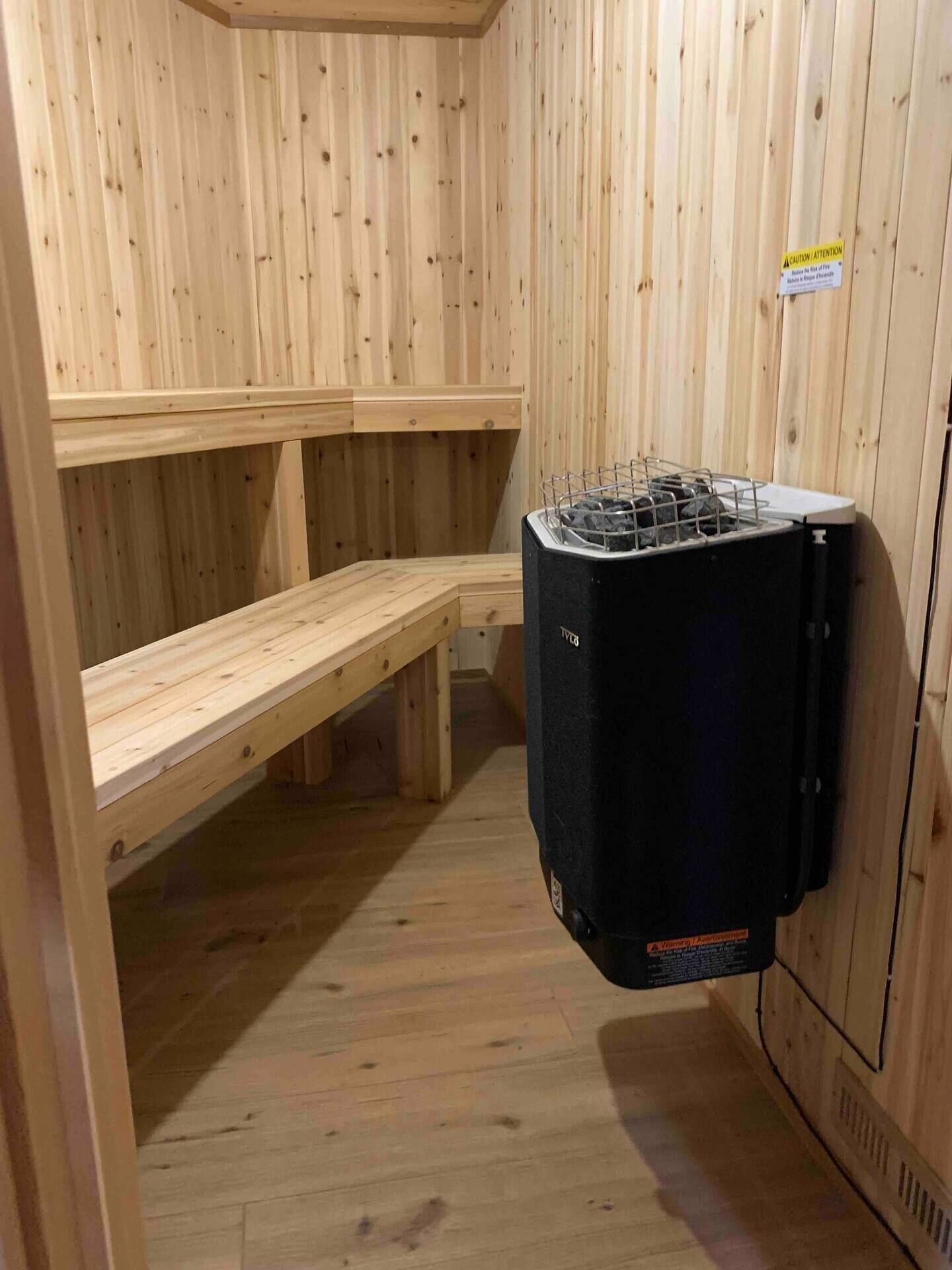 Uma sala de sauna com bancos de madeira e um aquecedor de sauna preto.