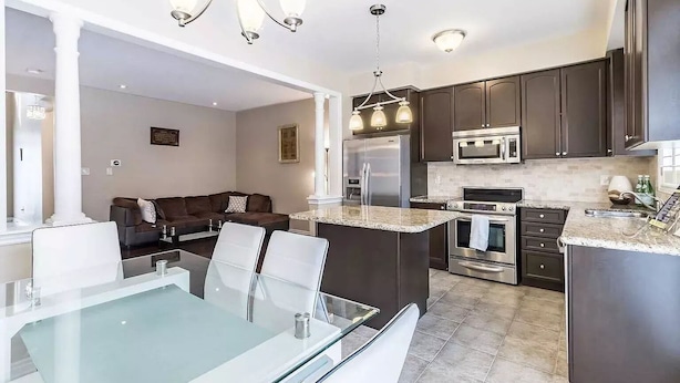 A modern kitchen with dark cabinets, stainless steel appliances, and a glass dining table. - Spacious and Comfortable House near Squireband (Mississauga)
