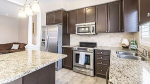 A modern kitchen with dark cabinets, stainless steel appliances, granite countertops, and a built-in oven. - Spacious and Comfortable House near Squireband (Mississauga)