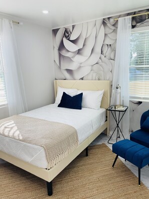 A modern bedroom with a large bed, a side table, a blue chair, and a wall with a floral pattern. - Private Lux Home - Separate Lounge - Backyard Oasis - Golf - Fire Pit (Charlotte)
