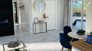Una sala de estar moderna con una mesa de centro de vidrio, un sillón azul, una mesa de comedor con sillas, una puerta blanca y un espejo grande en la pared.
