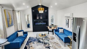 Una sala de estar moderna con sofás azules, una mesa de centro, un candelabro y un televisor grande.