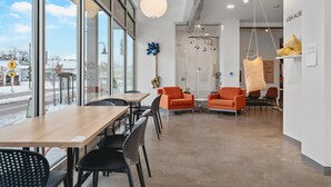 Et moderne interiør med et træbord og sorte stole, orange sofaer og en hængende lampe.