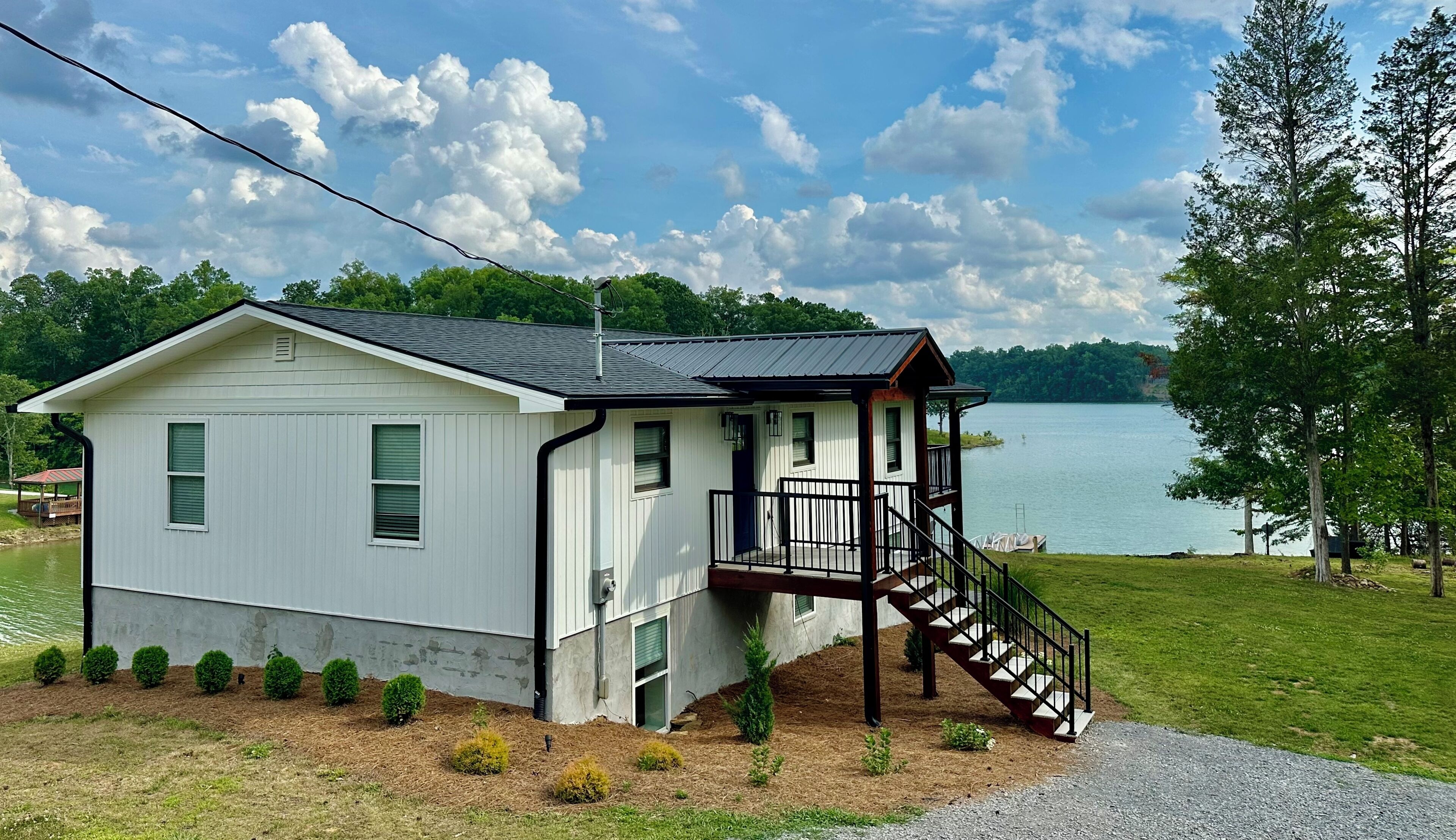 A white cabin with a balcony and stairs leading to a deck, overlooking a lake.