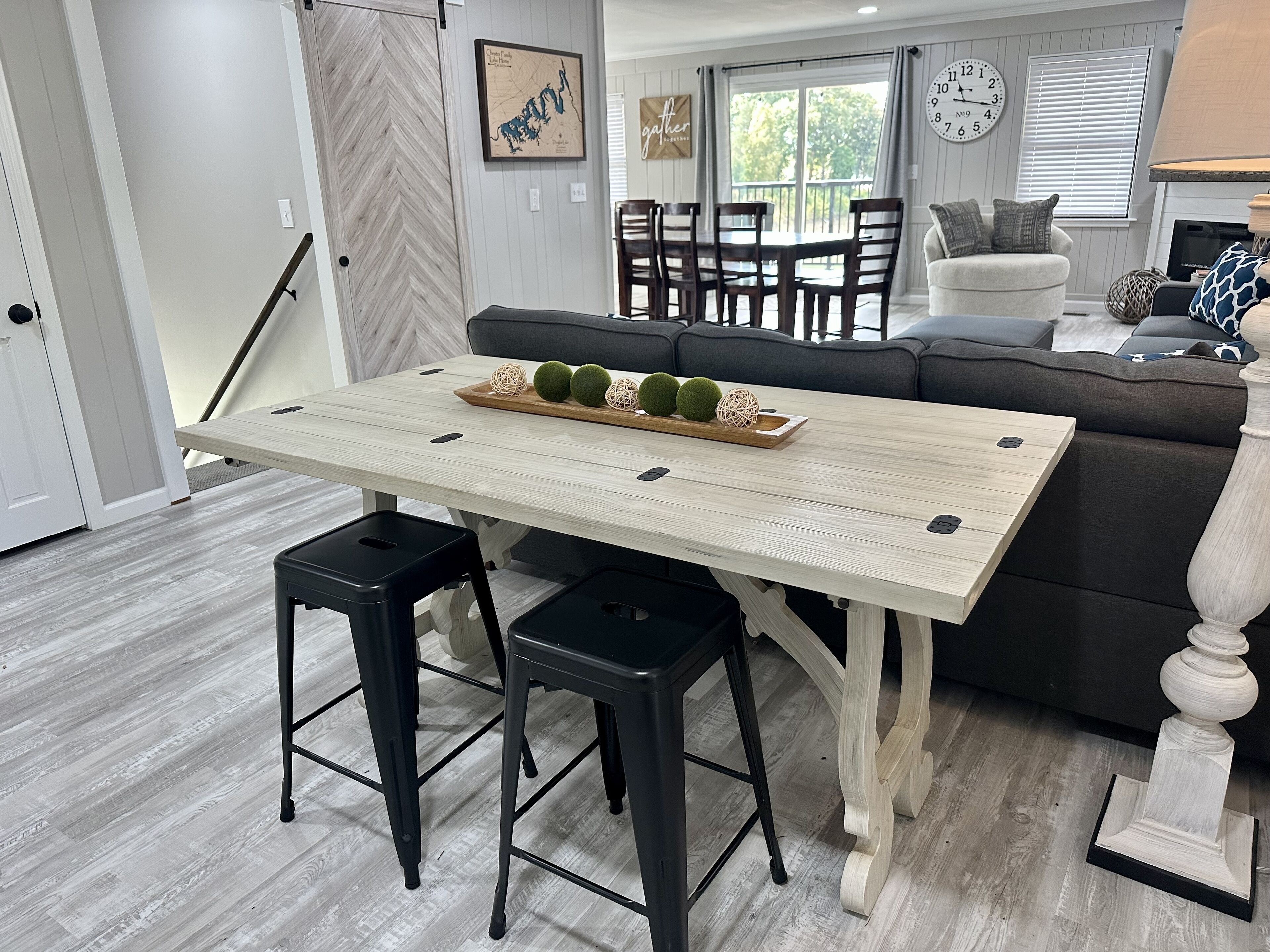Un espace repas comprenant une table en bois, des tabourets noirs et un plateau décoratif orné de sphères vertes.
