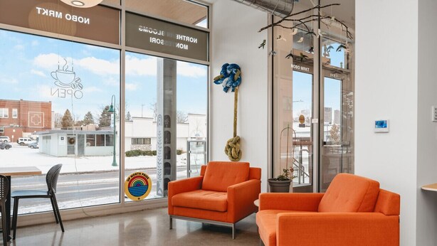 A modern interior with orange armchairs, a glass door with a view of the street, and a logo on the glass. - Fir Tree House 307 (Traverse City)