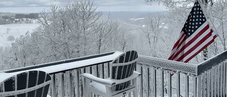 Ein mit Schnee bedeckter Balkon mit zwei Adirondack-Stühlen und einer amerikanischen Flagge.