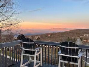 Eine Terrasse mit zwei Stühlen mit Blick auf eine Berglandschaft bei Sonnenuntergang.