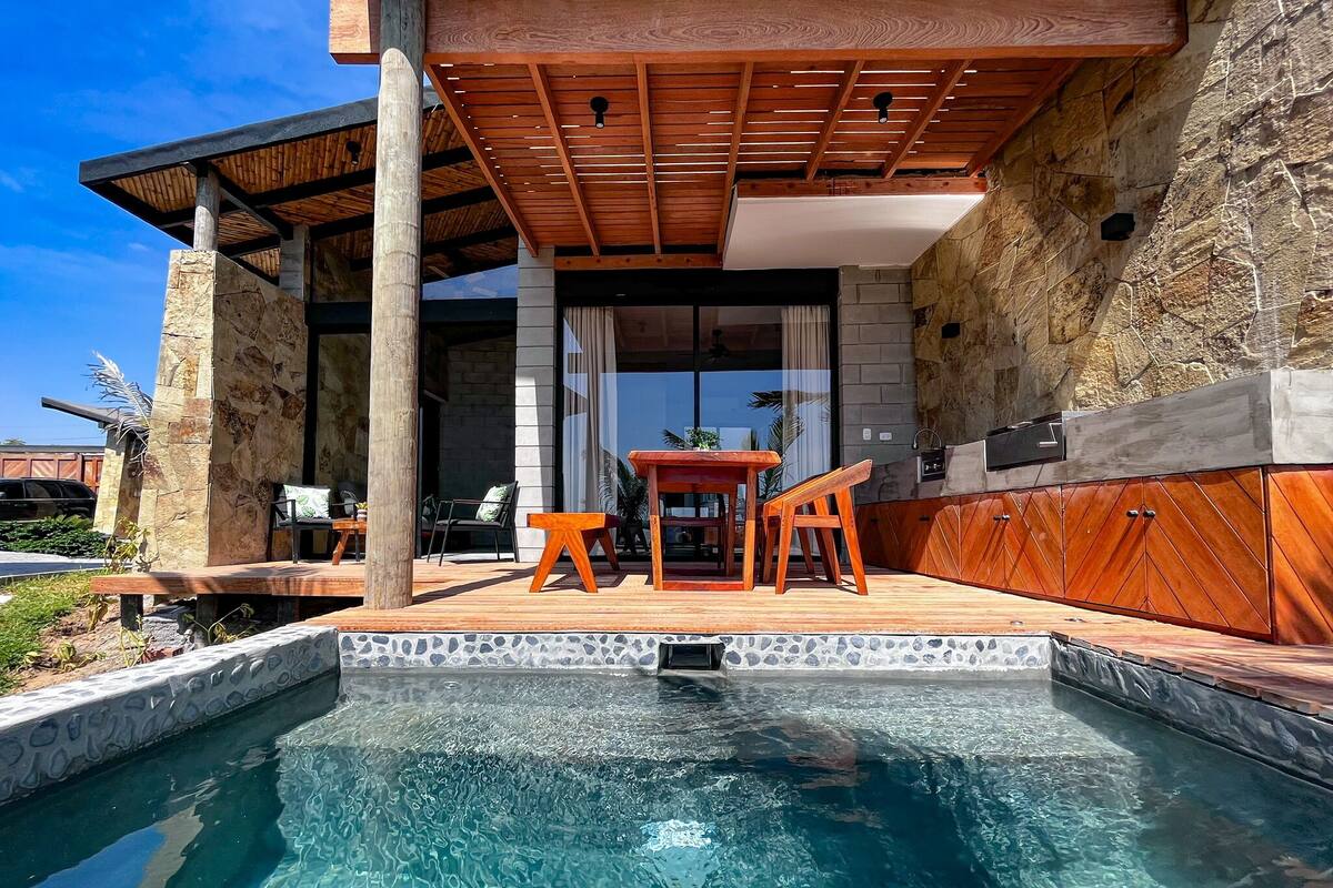 Un espace piscine doté d’une terrasse en bois, de murs en pierre et d’une cuisine extérieure moderne.