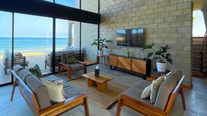 A spacious living area with a large window overlooking the ocean, a wooden ceiling, and a modern TV on the wall. - DIEM Vichayito Beachfront Eco-Luxury (Los Organos)