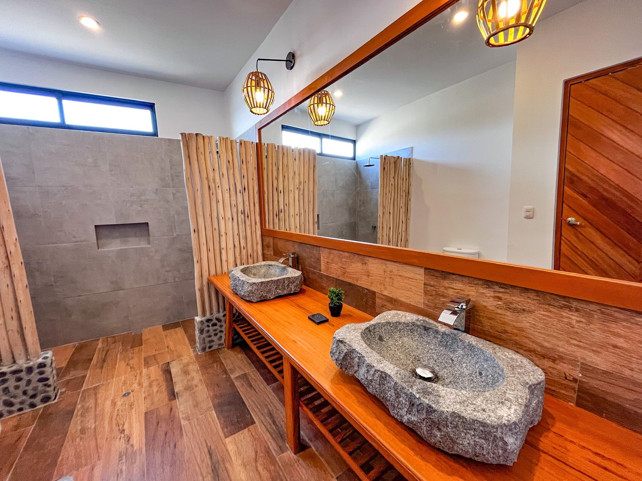 Un baño moderno con tocador de madera, dos lavamanos de piedra, un espejo grande y piso de madera.