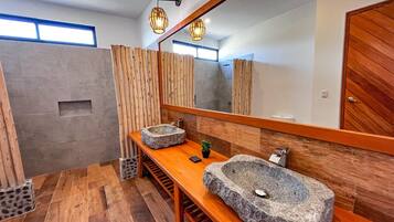 Un baño moderno con tocador de madera, dos lavamanos de piedra, un espejo grande y piso de madera.