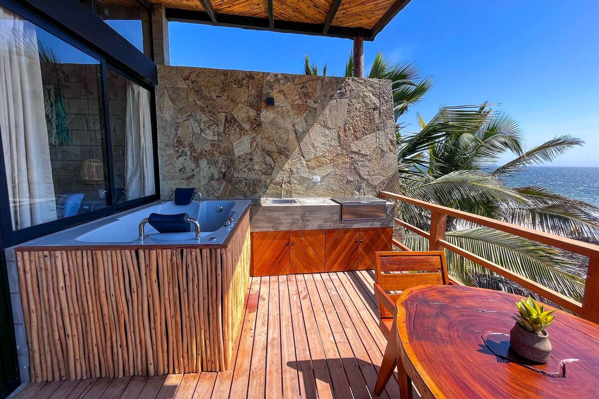 Une terrasse en bois avec un mur en pierre, un jacuzzi et une table agrémentée d’une plante en pot.