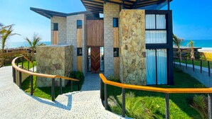 A modern coastal building with a stone facade, large windows, and a curved pathway leading to the entrance. - DIEM Vichayito Beachfront Eco-Luxury (Los Organos)