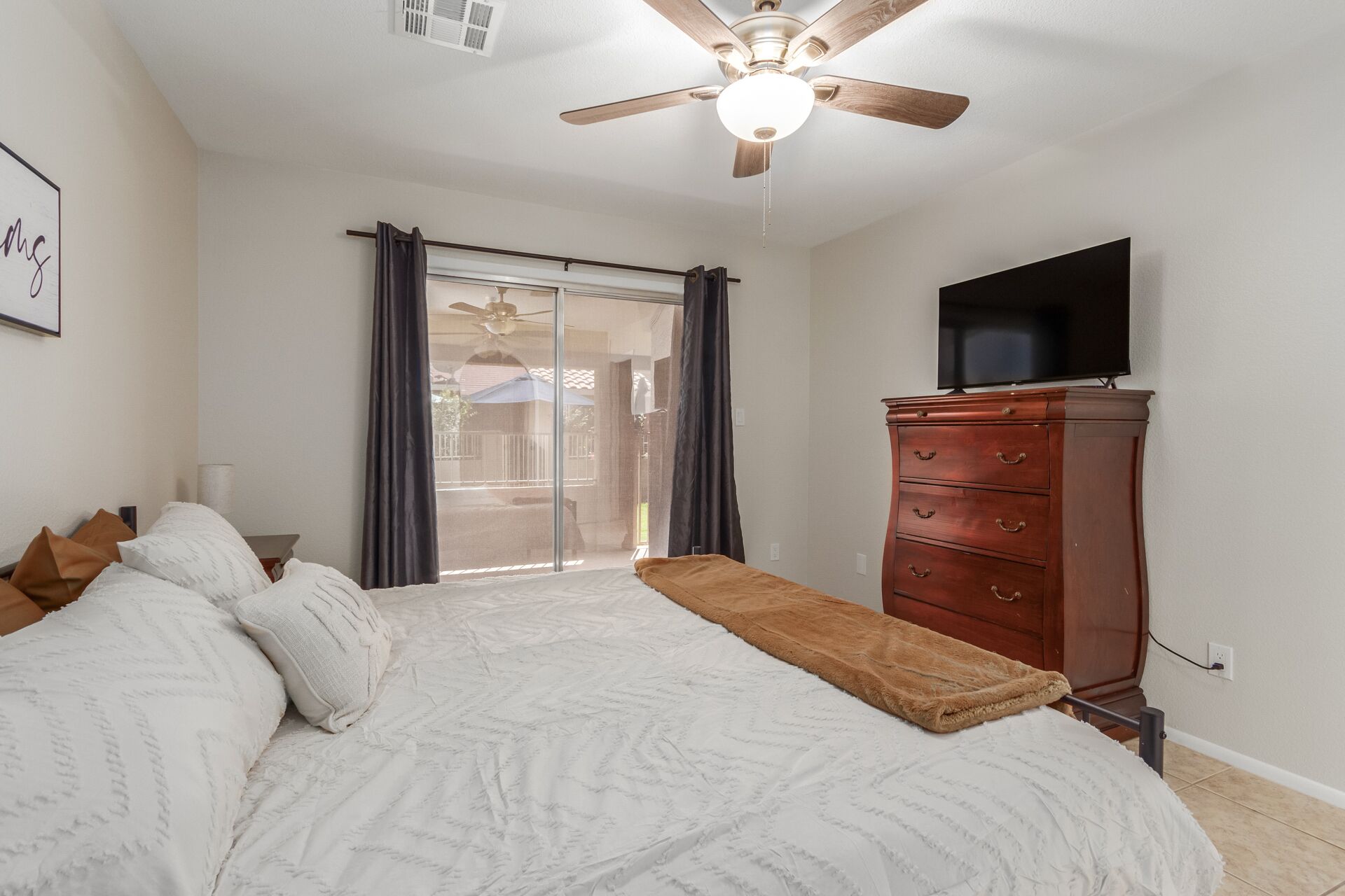 A bedroom with a bed, a ceiling fan, a TV, and a dresser.