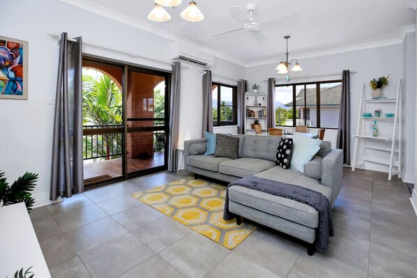 A modern living room with a grey sofa, a yellow patterned rug, and a ceiling fan.
