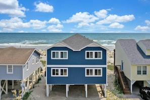 A beachfront property with a two-story house featuring a balcony, a covered porch, and a staircase leading to a second level.
