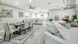 A modern kitchen with white cabinets, a stainless steel range hood, and a dining area with a white table and chairs.