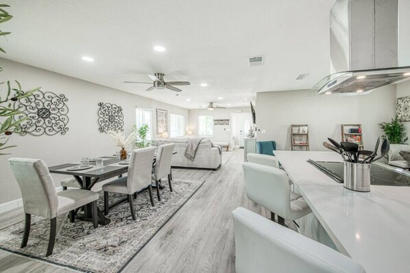 A modern kitchen with white cabinets, a stainless steel range hood, and a dining area with a white table and chairs.