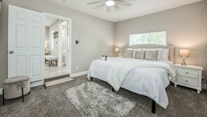 A bedroom with a bed, nightstands, a ceiling fan, and a door leading to another room.
