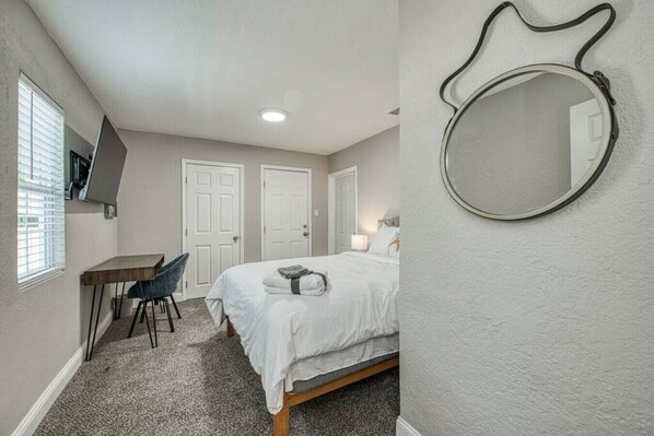 A bedroom with a bed, a desk, a chair, and a round mirror on the wall.