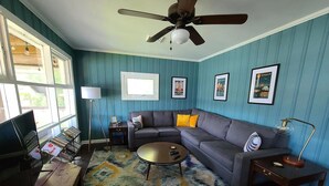 A living room with a sofa, coffee table, and a TV. There are framed pictures on the wall and a ceiling fan. - Private Riverfront Home with dock (Hague)
