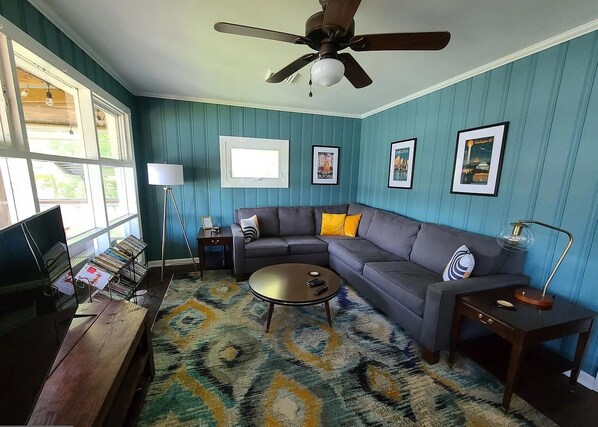 A living room with a sofa, coffee table, and a TV. There are framed pictures on the wall and a ceiling fan. - Private Riverfront Home with dock (Hague)