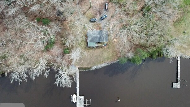 An aerial view of a lakeside property with a dock, a small house, and a parking area with three vehicles. - Private Riverfront Home with dock (Hague)