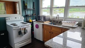 A kitchen with a stove, microwave, sink, and a window overlooking a body of water. - Private Riverfront Home with dock (Hague)