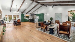 A spacious loft with exposed wooden beams, a dining area, a living room with a sofa and chairs, and a kitchen with green cabinets. - 6 Mins from Main St, Hot tub, Chef's Kitchen! (Fredericksburg)
