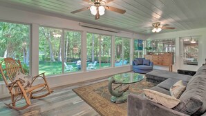 A spacious living room with large windows, a ceiling fan, and a mix of seating including a rocking chair and a sofa. - Withlacoochee River Chalet Great River View, near Rainbow River (Dunnellon)