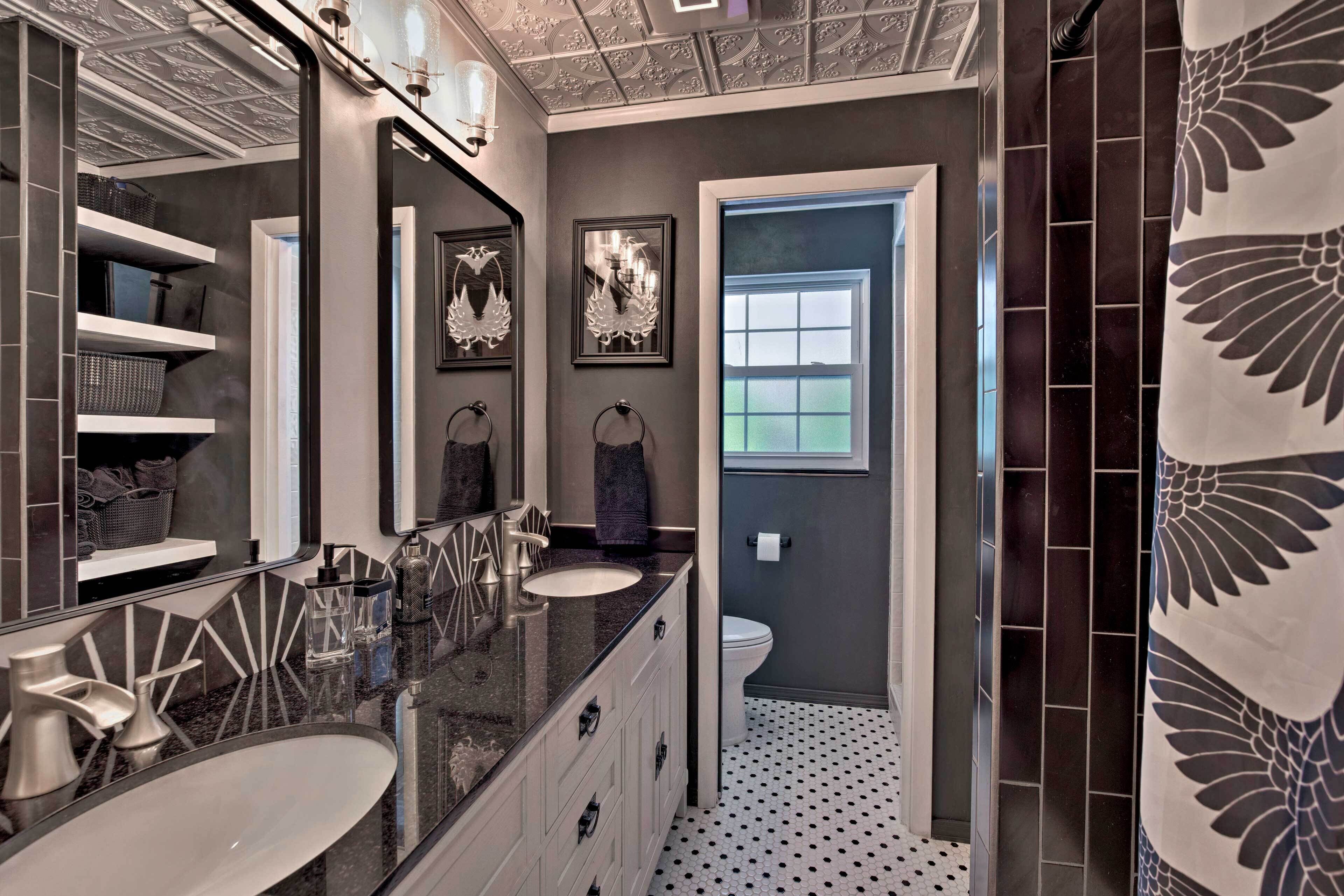 A bathroom with a large mirror, two sinks, a toilet, and a window.