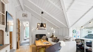 A cozy, well-lit room with a wooden dining table, a comfortable sofa, and a white armchair.