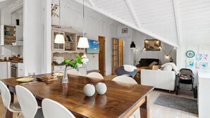 A spacious living area with a wooden dining table, white chairs, and a cozy seating area with a sofa and armchairs.