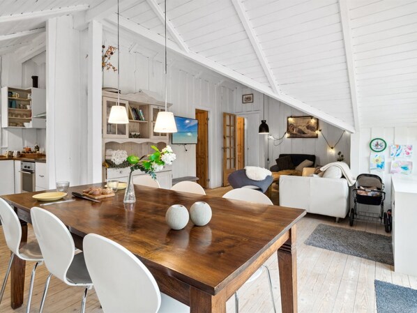 Amplia sala de estar con mesa de comedor de madera, sillas blancas y una zona de estar acogedora con sofá y sillones.